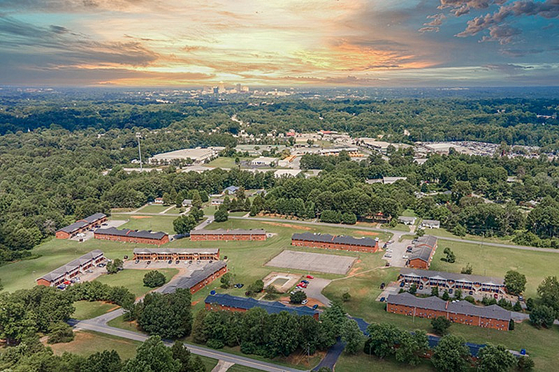 Breathtaking aerial view of a peaceful residential community surrounded by lush greenery, under a vibrant sunset sky.