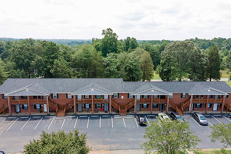 Charming brick apartment complex set amid lush greenery, featuring convenient parking and inviting balconies.