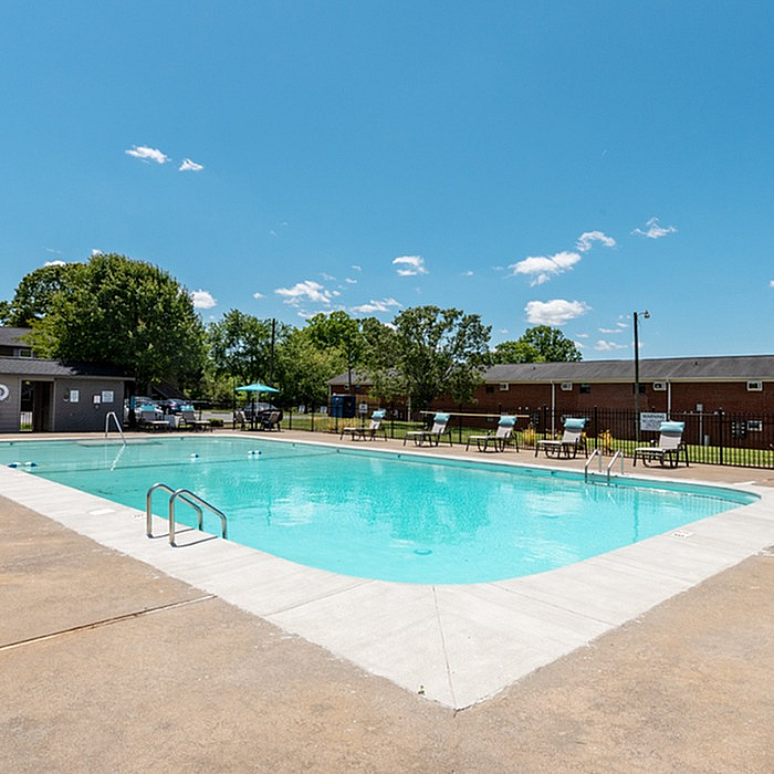 Inviting community pool area with clear blue water, surrounded by sun loungers and lush greenery, perfect for a relaxing summer day.