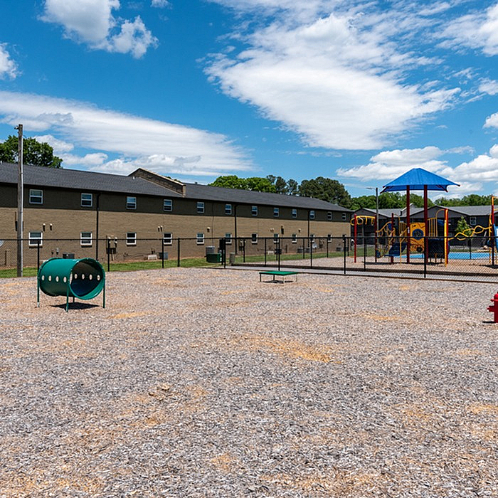 Vibrant community playground with modern play structures, surrounded by a spacious open area and residential buildings under a bright blue sky.