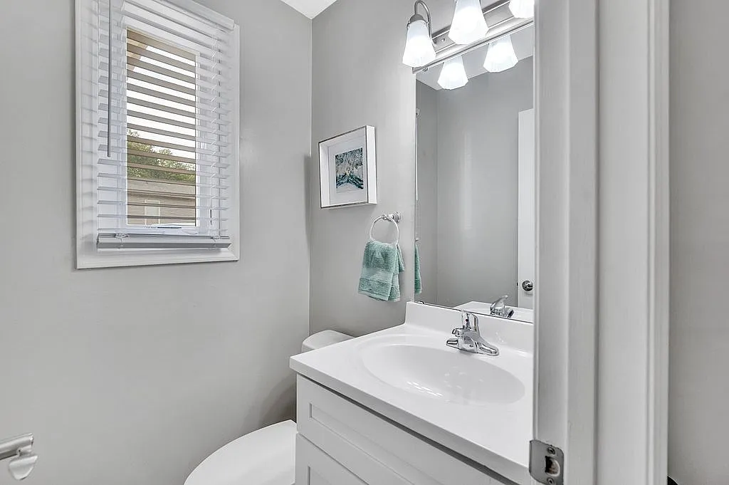 Modern bathroom with sleek white vanity, polished fixtures, and natural light streaming through a window with blinds.