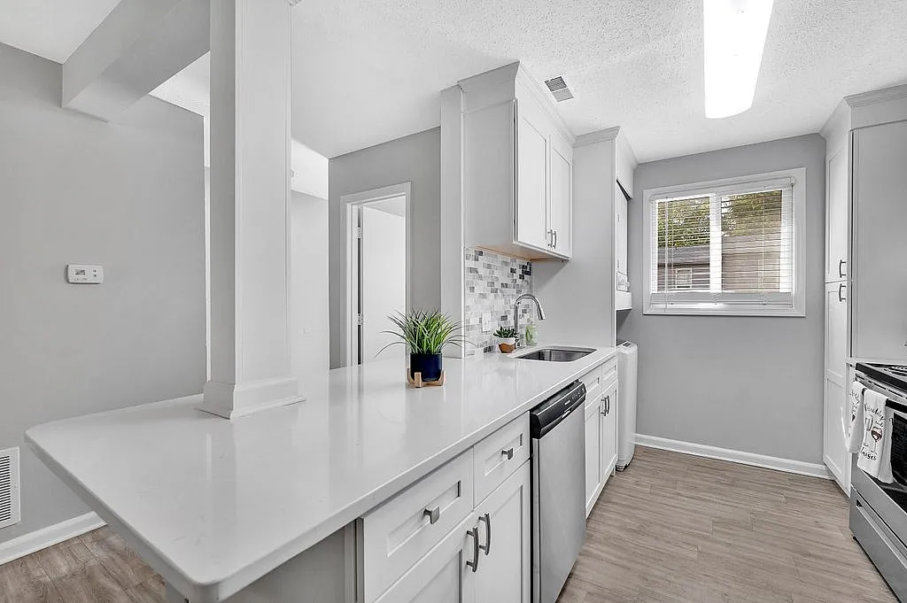 Chic kitchen with modern white cabinetry, elegant countertops, stainless steel appliances, and natural light streaming through a large window.