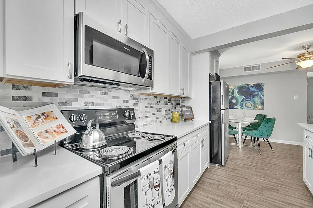 Modern kitchen with sleek stainless steel appliances, elegant white cabinetry, stylish backsplash, and an inviting adjacent dining area with vibrant green chairs.