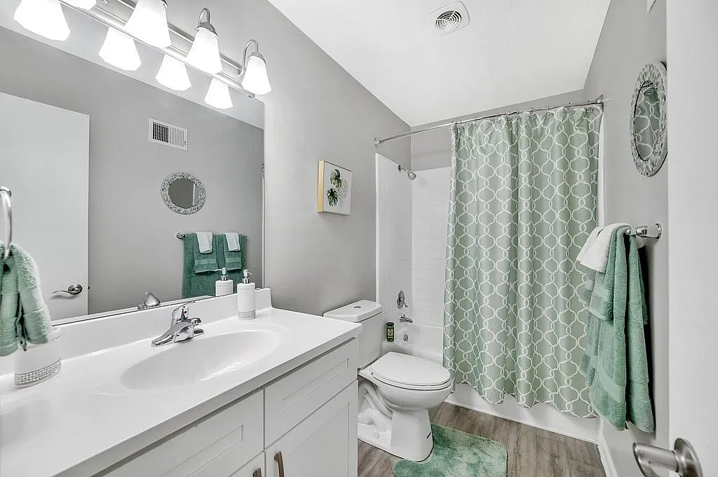 Elegant bathroom featuring a sleek white vanity, modern fixtures, and a soothing green color theme with patterned shower curtain and matching towels.