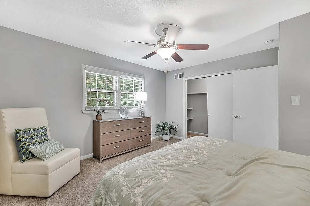 Inviting bedroom with plush bedding, modern dresser, and serene natural light enhancing the tranquil atmosphere.