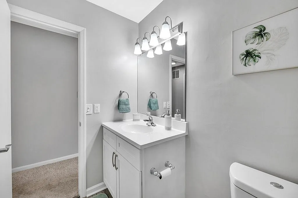 Elegant bathroom with modern white vanity, stylish lighting fixtures, and calming green accents, creating a serene ambiance.