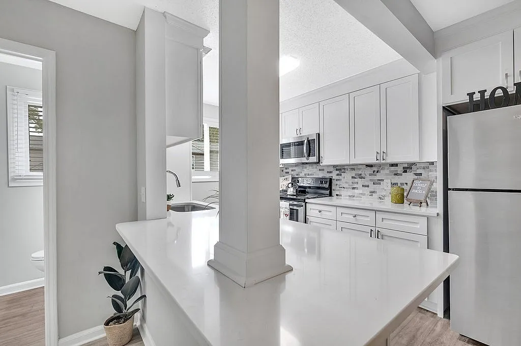 Bright, modern kitchen featuring sleek white cabinets, stylish tiled backsplash, and stainless steel appliances, creating a welcoming cooking space.