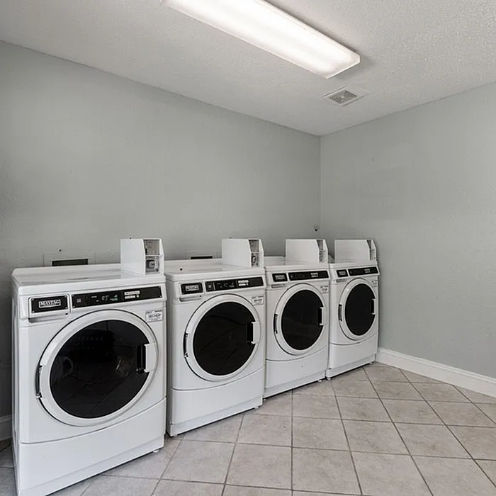 Modern laundry room with four sleek white washing machines set against a calming light grey wall, perfect for convenient living.