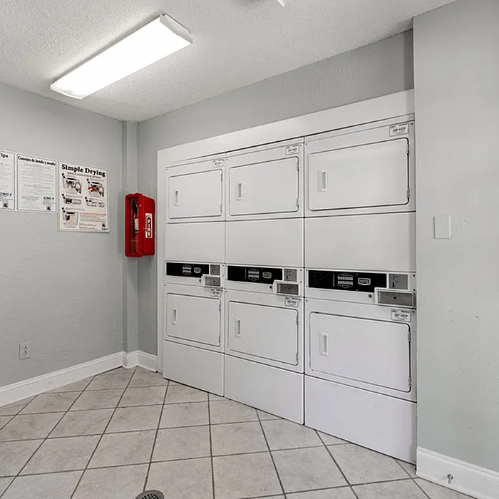 Bright and efficient laundry room with modern, stacked washers and dryers, tiled flooring, and clear usage instructions for convenience.