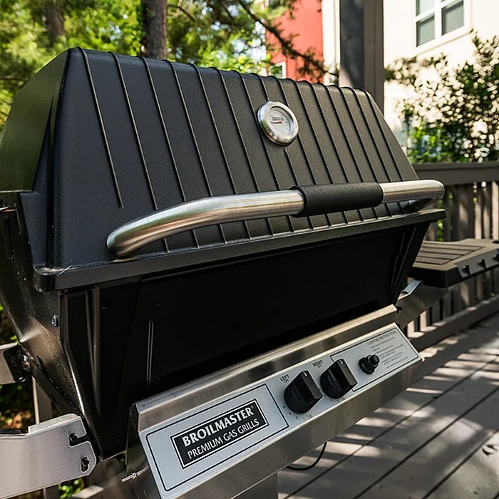 Elegant outdoor Broilmaster gas grill on a stylish deck, surrounded by lush greenery, perfect for a luxurious cooking experience.