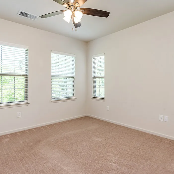 Bright and airy room with plush carpeting and large windows, enhanced by a modern ceiling fan.