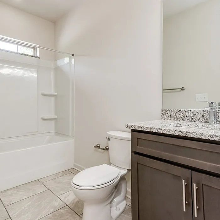 Modern bathroom with elegant granite countertop, sleek cabinetry, and a spacious bathtub with glass enclosure.