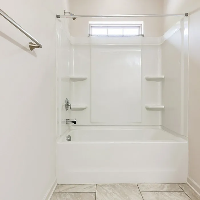 Modern bathroom with pristine white bathtub and shower, accented by elegant tile flooring and natural light from a frosted window.