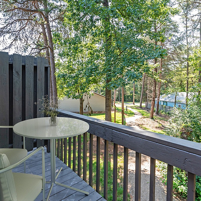 Charming balcony with a cozy table set overlooking lush greenery and a peaceful path.