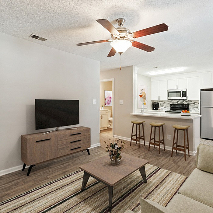 Bright and modern living room with ceiling fan, cozy seating, TV stand, and open kitchen with barstools for a welcoming atmosphere.