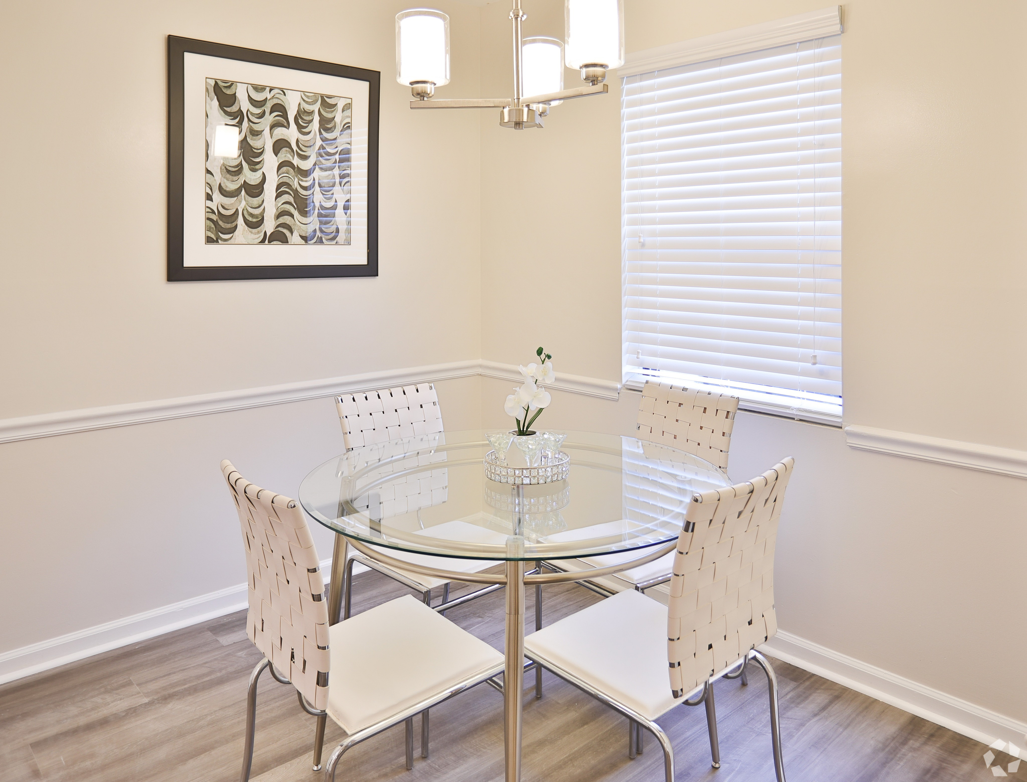 Chic dining area with a modern glass table, stylish white chairs, and elegant wall art, basking in natural light.