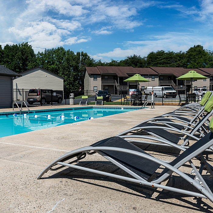 Inviting swimming pool area with sleek lounge chairs under a vibrant blue sky, perfect for relaxation in a stylish apartment complex.