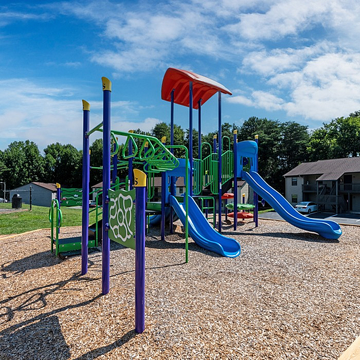Bright and inviting playground with colorful slides and climbing structures, nestled in a scenic residential area under a clear blue sky.