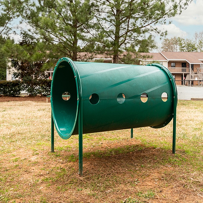 Inviting green playground tunnel surrounded by lush greenery and residential buildings, perfect for outdoor activities.