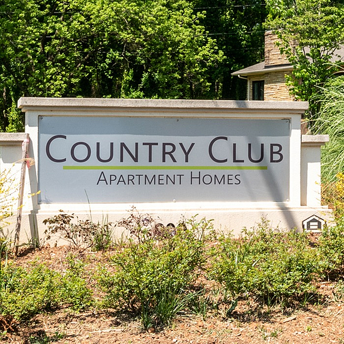 Charming entrance to Country Club Apartment Homes surrounded by lush greenery and natural beauty.
