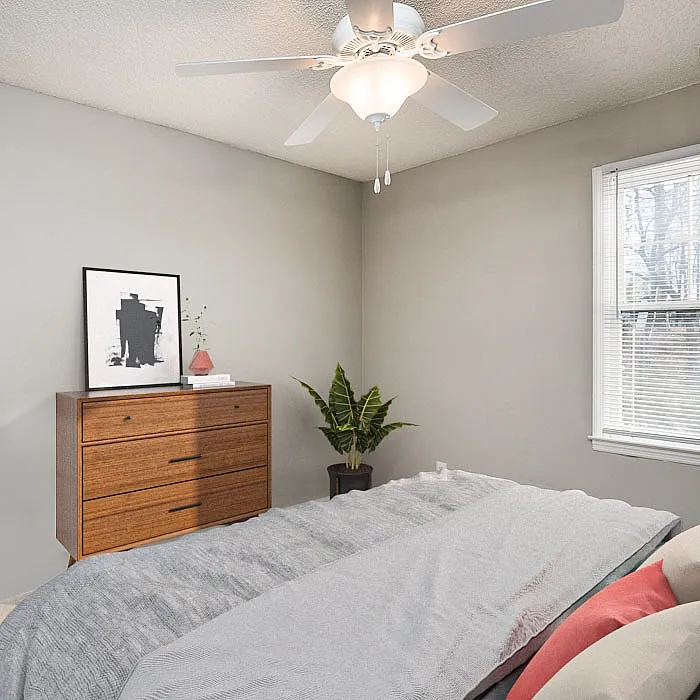 Cozy bedroom with modern ceiling fan, natural light, stylish dresser, and accent plant creating a serene atmosphere.