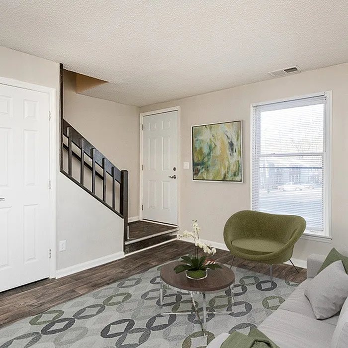 Inviting living room featuring modern decor, elegant staircase, and large window with ample natural light.