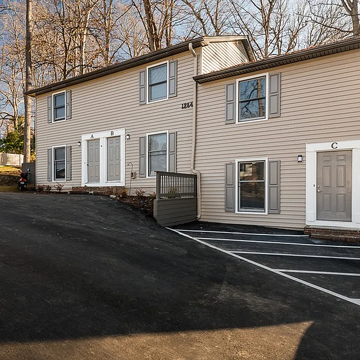 Charming duplex exterior showcasing modern siding, individual entrances, and convenient parking spaces in a serene natural setting.