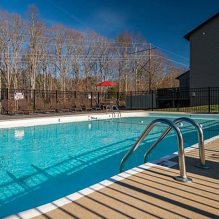 Inviting outdoor swimming pool with lounge chairs and fenced railing, surrounded by scenic trees on a sunny day.