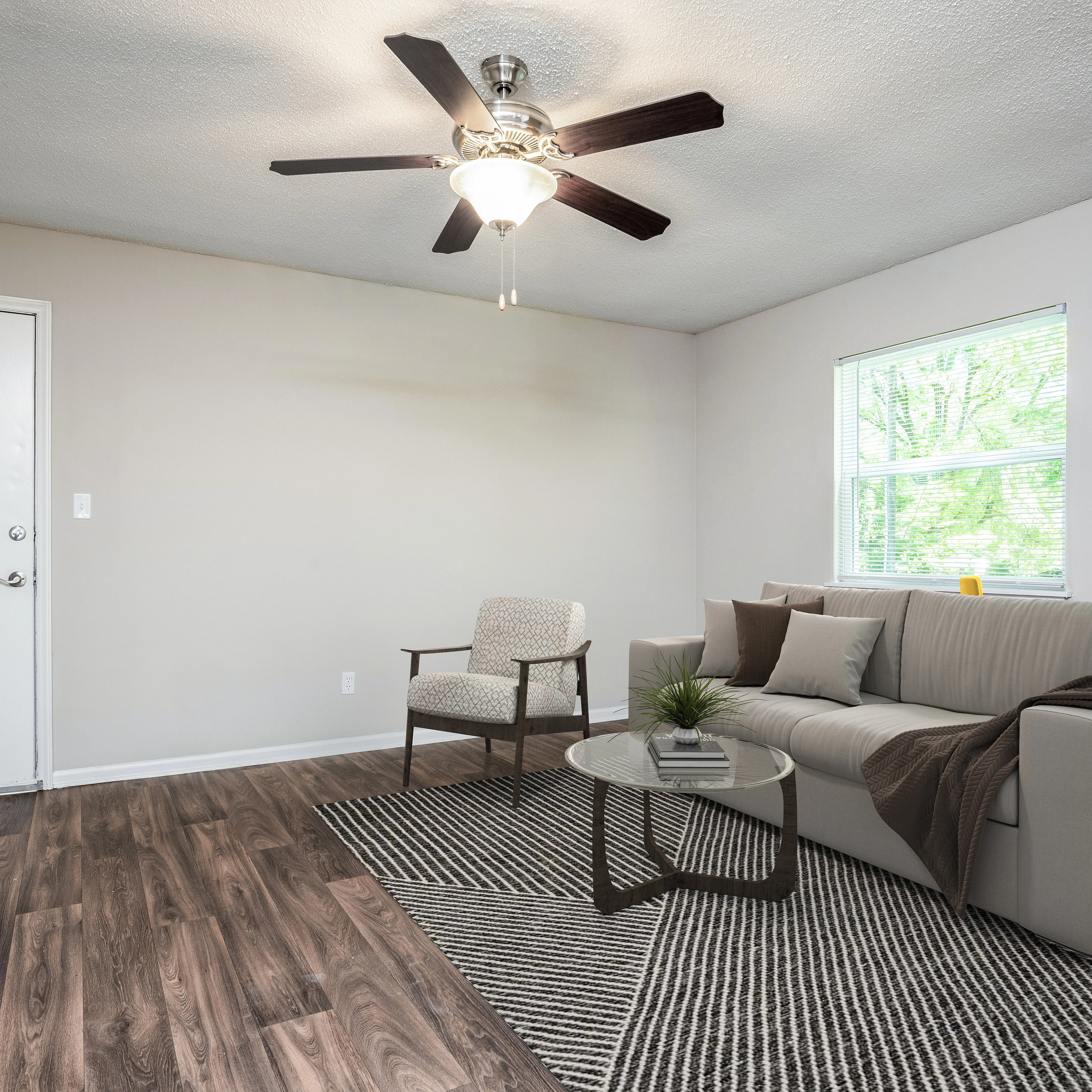 Inviting living room with modern ceiling fan, elegant hardwood floors, and cozy seating arrangement bathed in natural light.
