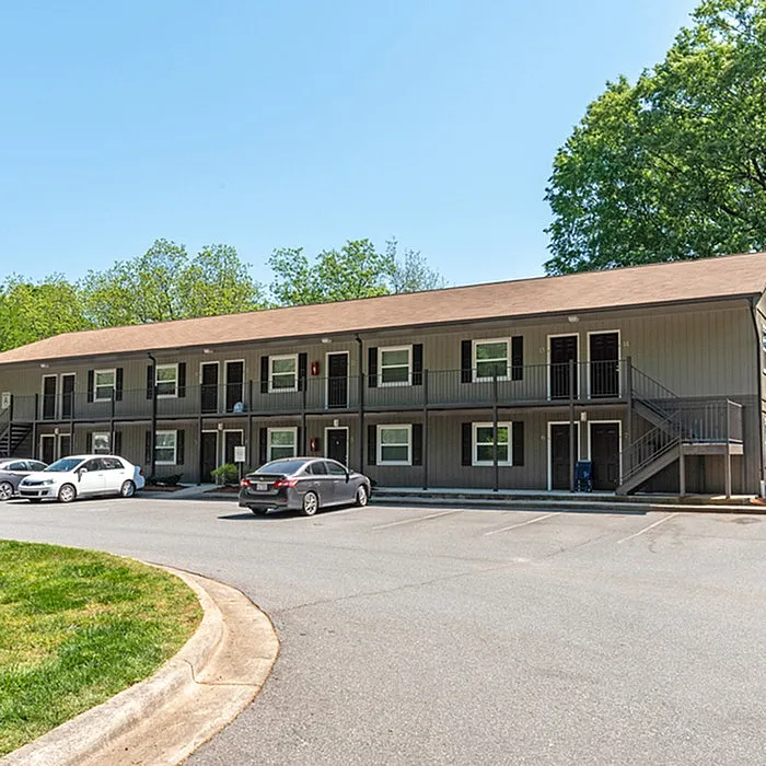 Charming two-story apartment complex with spacious parking and lush green surroundings.