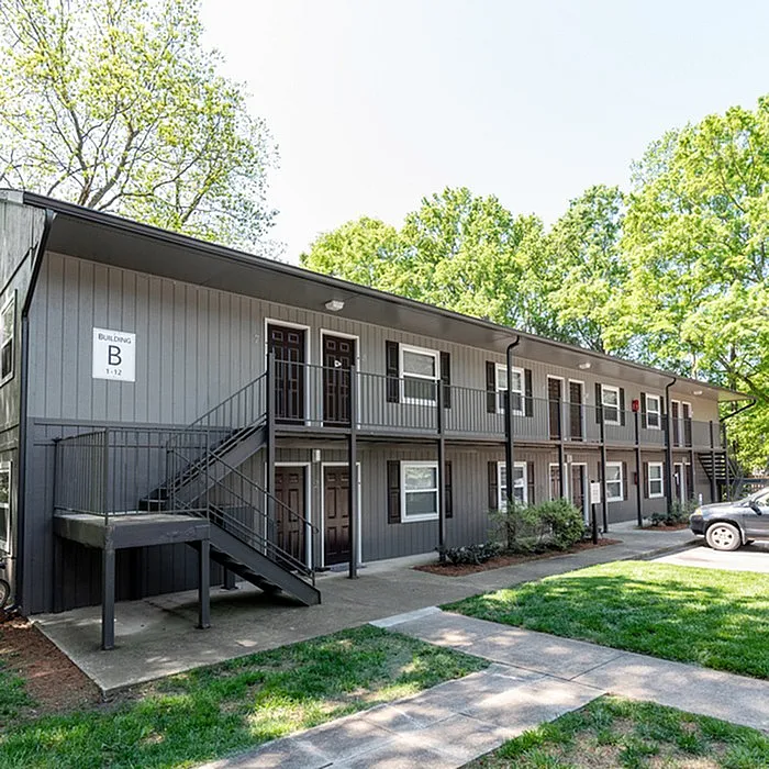 Charming two-story apartment building surrounded by lush greenery, featuring modern exterior and ample parking space.