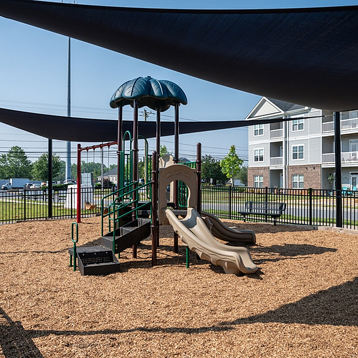 Inviting outdoor playground with modern slides and climbing structure, shaded by elegant canopies, located near charming apartment buildings.