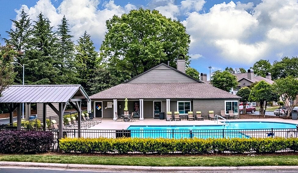 Inviting apartment community with a sparkling pool, ample seating, and lush greenery, perfect for relaxation and leisure.