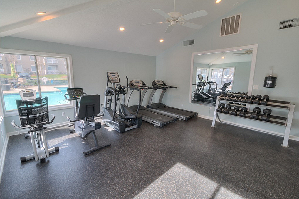 Bright and modern fitness room with treadmills, exercise bike, and free weights, overlooking a sparkling outdoor pool.