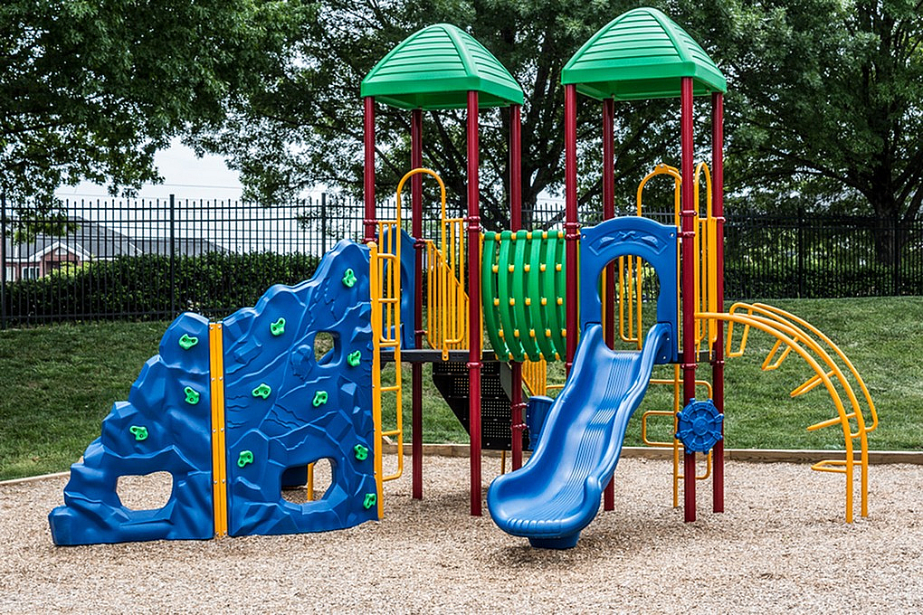 Vibrant playground with colorful climbing wall, slide, and tunnels set amidst lush greenery.