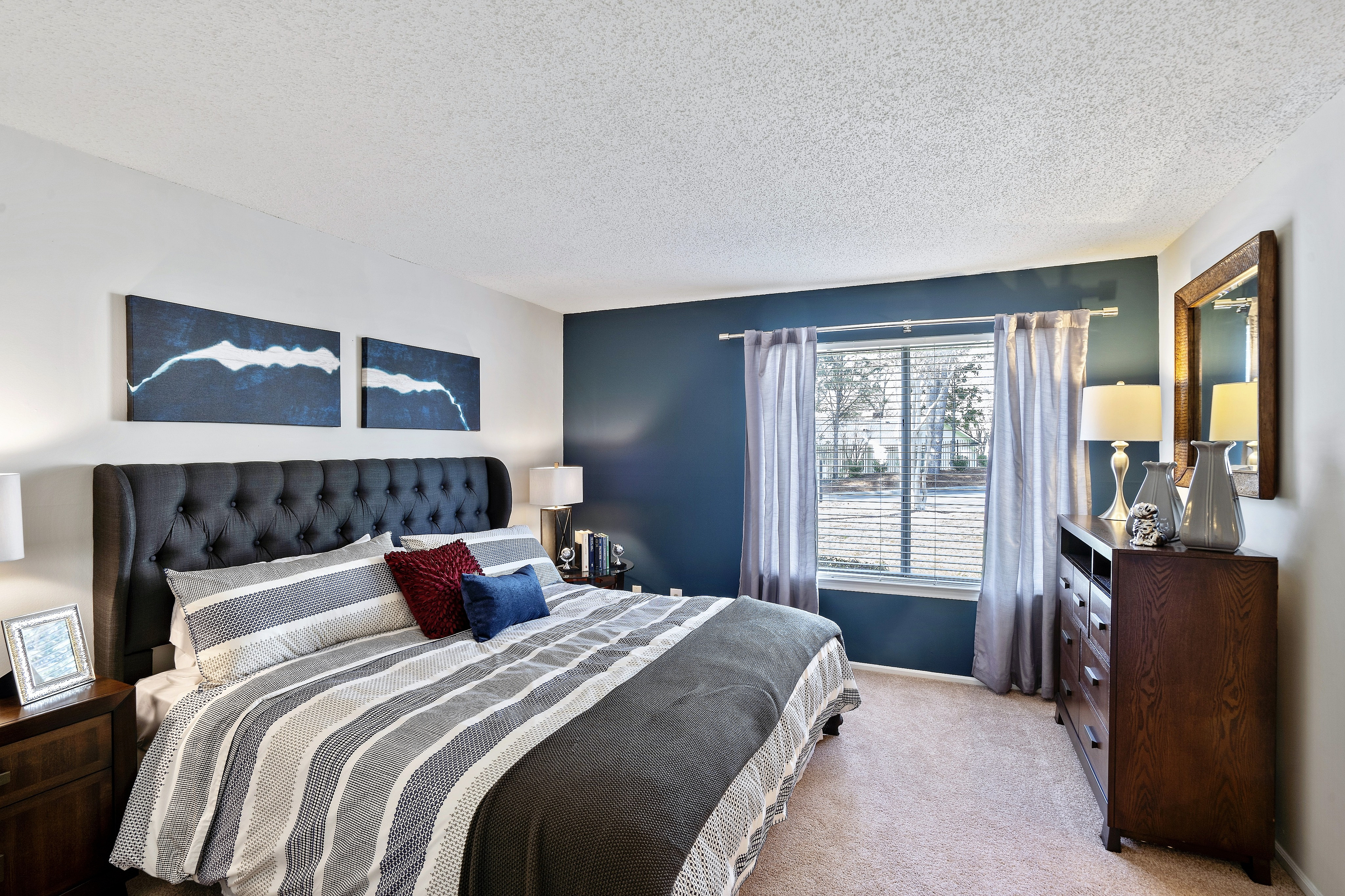 Inviting bedroom with a plush tufted headboard, stylish bedding, and a sunlit window offering serene views.