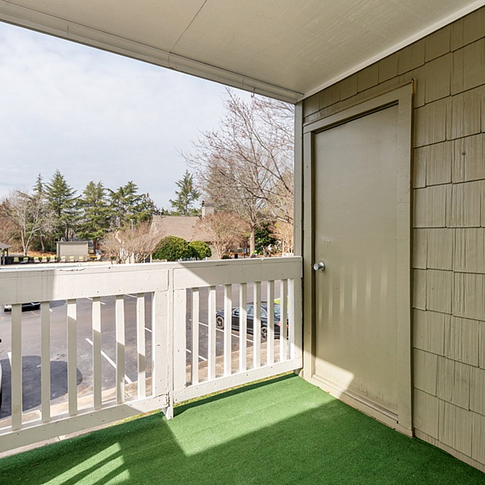 Charming apartment balcony with green artificial grass and scenic view of trees and open sky.