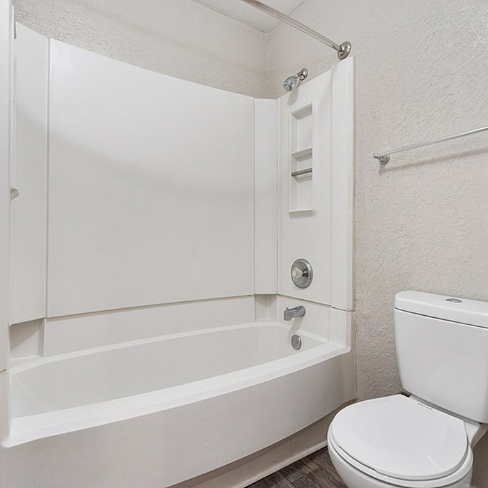 Modern bathroom featuring a pristine white bathtub with built-in shelves, sleek shower fixtures, and a contemporary toilet, offering a clean and inviting space.