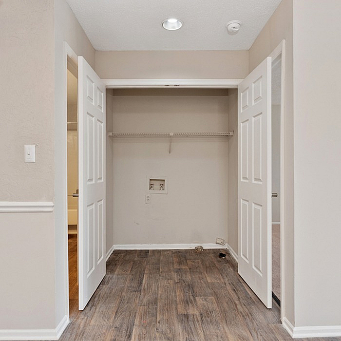 Charming laundry nook with double doors, featuring stylish wood flooring and ample shelving space.