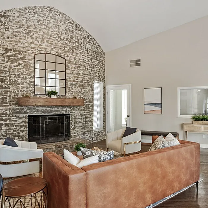 Chic living room with a rustic brick accent wall, stylish leather sofa, and plush armchairs surrounding a cozy fireplace.