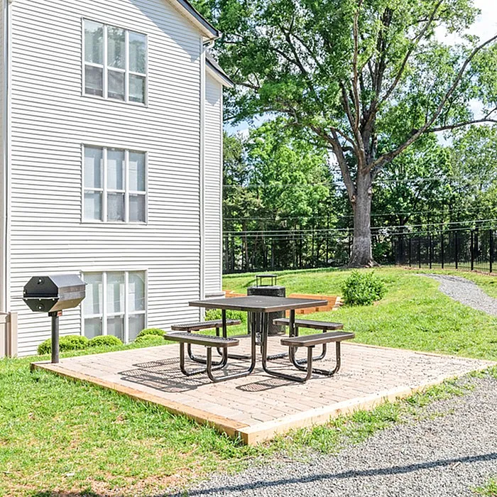Charming outdoor space featuring a picnic area with a grill, nestled beside a modern apartment building surrounded by lush greenery.