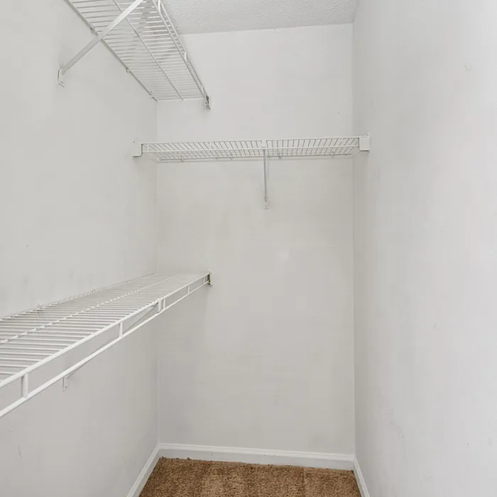 Spacious walk-in closet with sleek white wire shelving and plush carpet flooring, perfect for organized living.