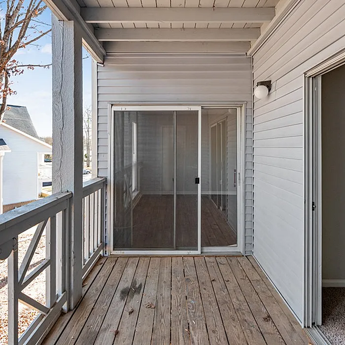 Charming sunlit balcony with sliding glass doors, featuring wood flooring and modern design.