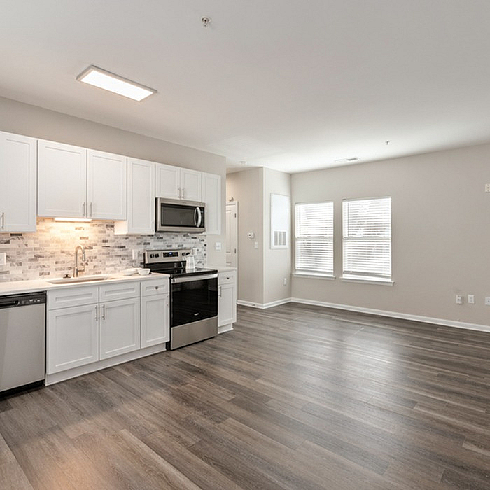 Modern open-concept kitchen and living area with sleek stainless steel appliances, elegant white cabinetry, and stylish wood flooring.