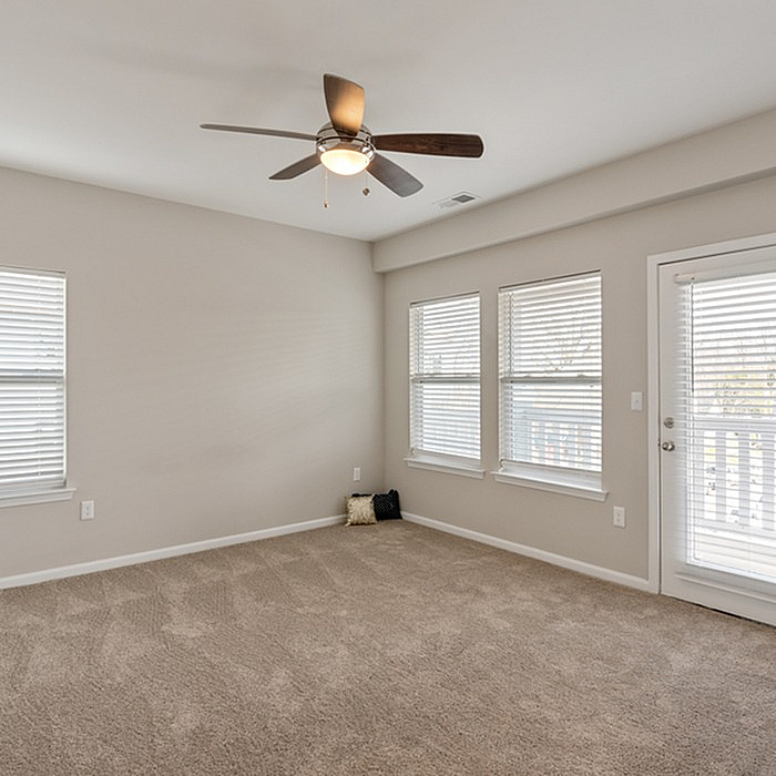 Bright and spacious bedroom featuring plush carpet, large windows with blinds, and a ceiling fan for comfort and style.