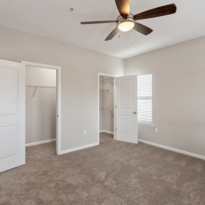 Cozy bedroom with lush carpet, elegant ceiling fan, and bright natural light from large window.