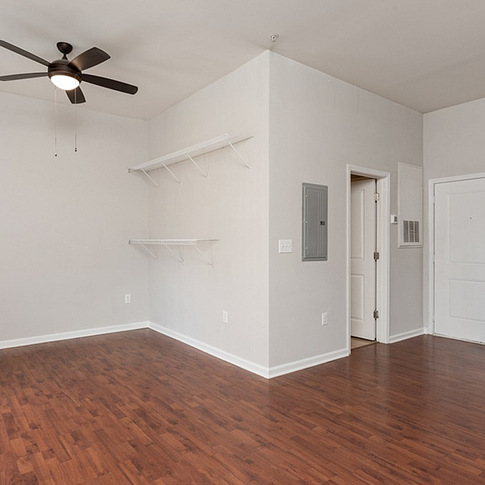 Modern apartment interior with sleek ceiling fan and rich wood flooring, featuring minimalist wall shelves and neutral walls for a spacious and airy feel.