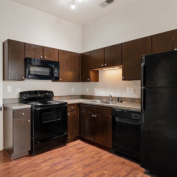 Modern kitchen with sleek dark wood cabinetry, black appliances, and warm wood flooring.