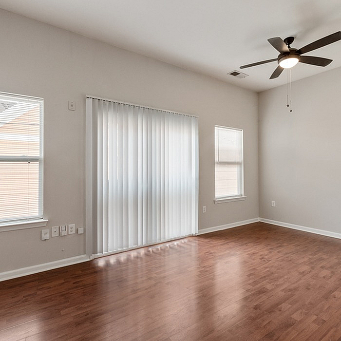 Bright and spacious living area with elegant hardwood floors, large windows, and modern ceiling fan.
