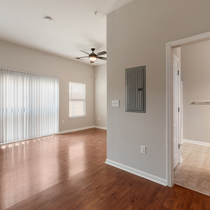 Bright and airy living space with sleek wooden floors, contemporary ceiling fan, and ample natural light through vertical blinds.
